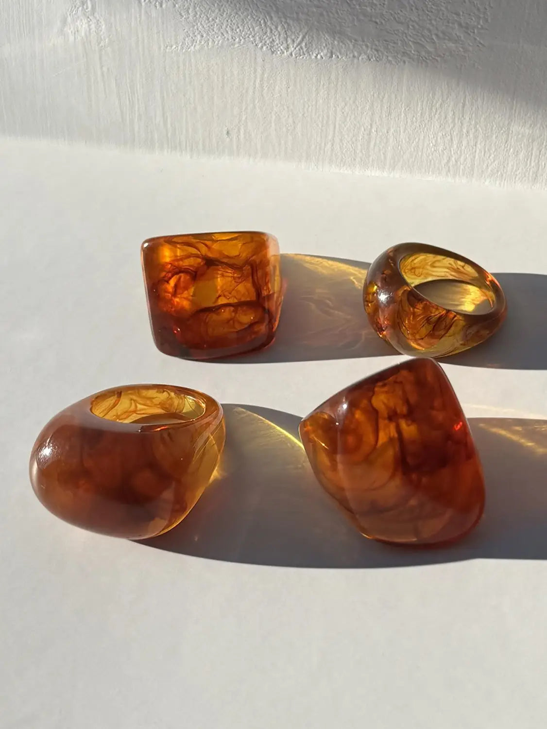 Four amber-colored translucent resin chunky cocktail rings with swirling golden and orange patterns in a 4-piece set.