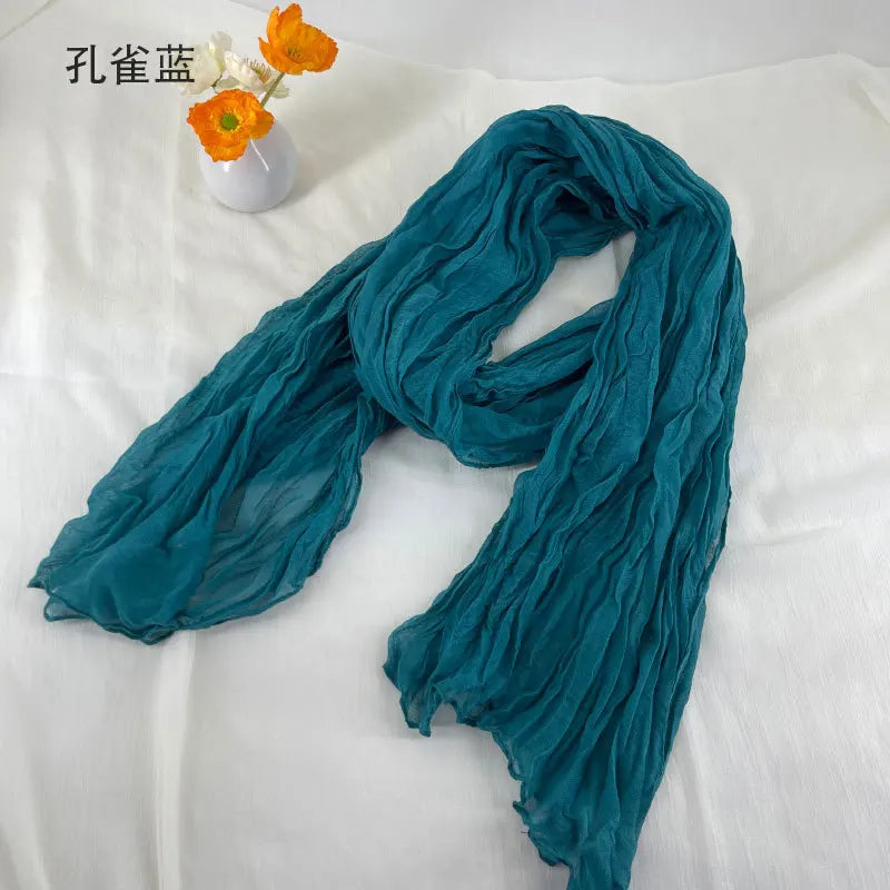Écharpe en coton et lin plissé turquoise douce, avec une texture froissée délicate et des bords légèrement effilochés.