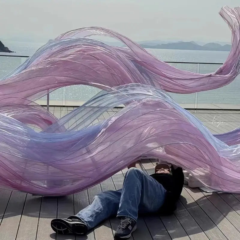 un telón decorativo de guirnalda floral gigante de gasa que presenta un fondo decorativo con forma de flor, con una escultura translúcida fluida en tonos degradados de lavanda y lila claro, con un acabado brillante