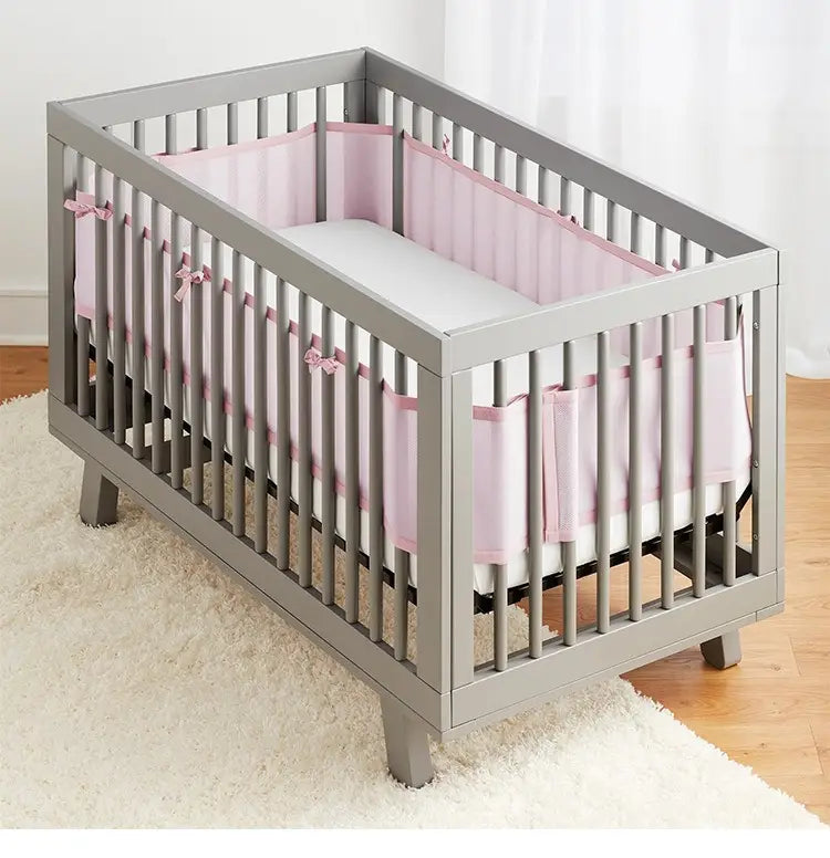 Graues Holz-Kinderbett mit atmungsaktiven Mesh-Polstern in Rosa als Stoßschutz mit dekorativen Schleifen für Teddy-Bären-Bettwäsche.