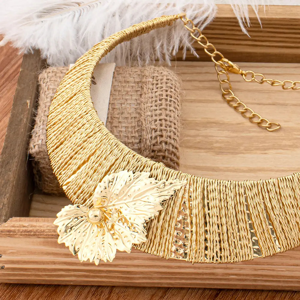 Parure de bijoux en perles et feuilles d’or, comprenant un collier ras du cou en maille tissée complexe de couleur dorée, avec un pendentif détaillé en forme de feuille et un accent de perle centrale.