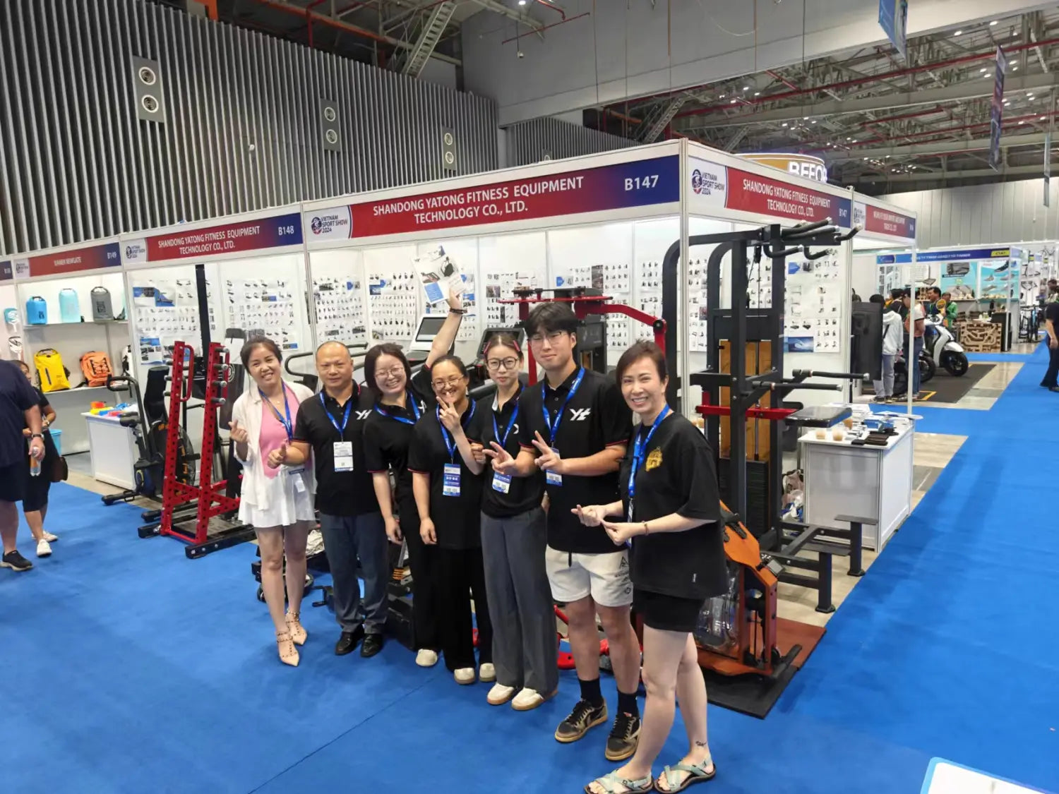 Group of seven people in matching black shirts and lanyards posing together at a commercial stair climber machine cardio stepmill fitness equipment trade show booth.