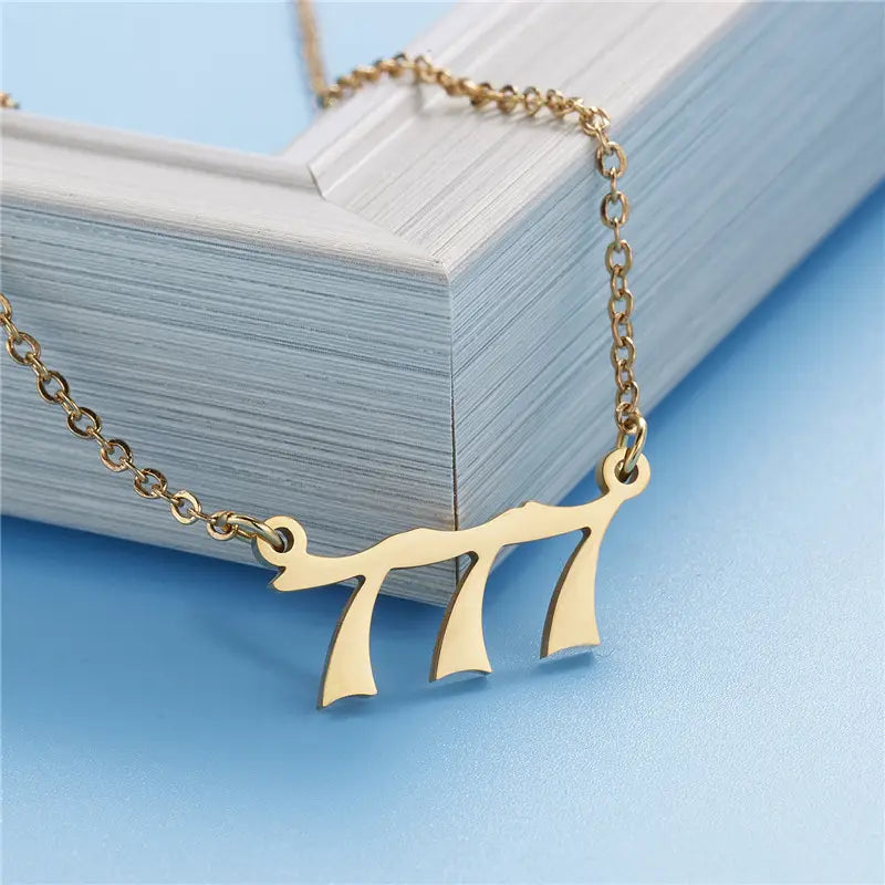 Gold angel number 7 necklace featuring a gold-colored delicate chain with a pendant shaped like the Hebrew letter shin.