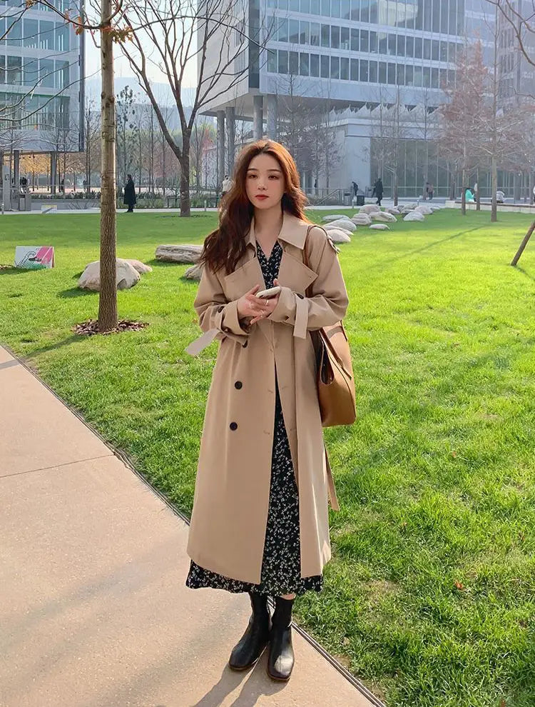Women double breasted trench coat in beige with black buttons and a belted waist suitable for formal wear.