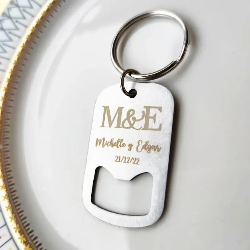 結婚式の引き出物向けに、刻印された金文字の「michelle」と「edgar」、日付「21/12/22」を施した、洗練されたシルバードッグタグ型のパーソナライズボトルオープナー用キーチェーン。クラシックなキーリングの取り付け具付き。