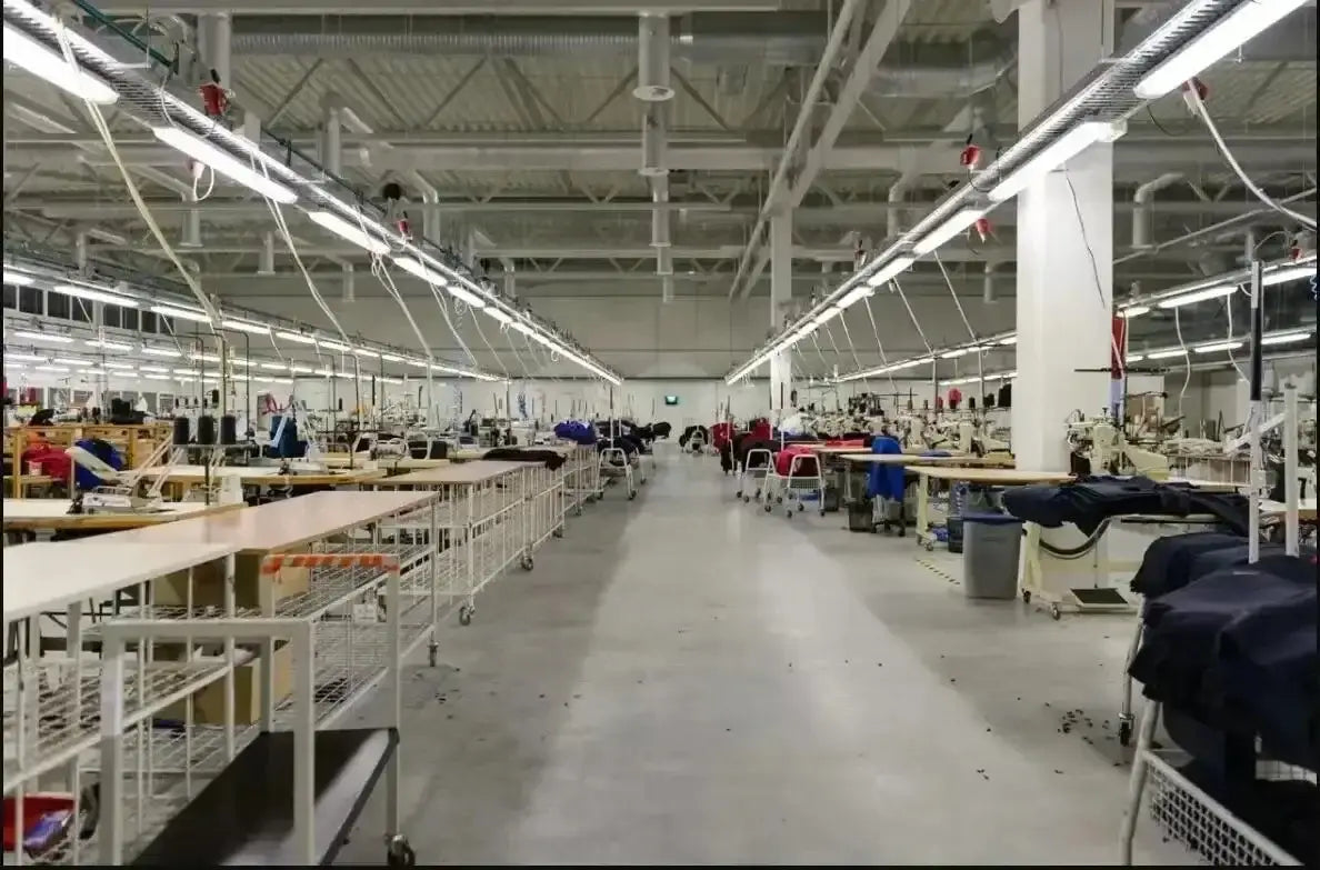 Reihen industrieller Nähmaschinen mit weißen Metallrahmen und schwarzer Polsterung arbeiten in einer hell beleuchteten Fabrik, die Tactical-Angel-Graphic-Cotton-T-Shirts herstellt.