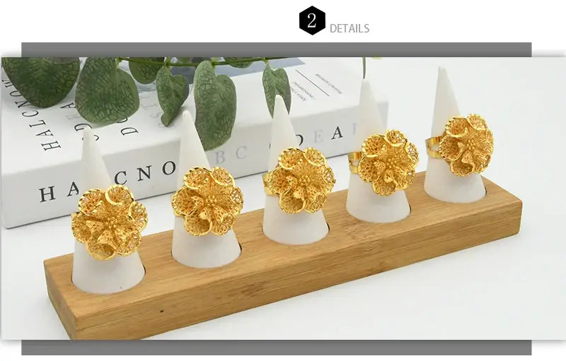 five ornate 24k gold plated flower rings displayed on white cone holders arranged in a wooden tray showcasing dubai jewelry designs for women