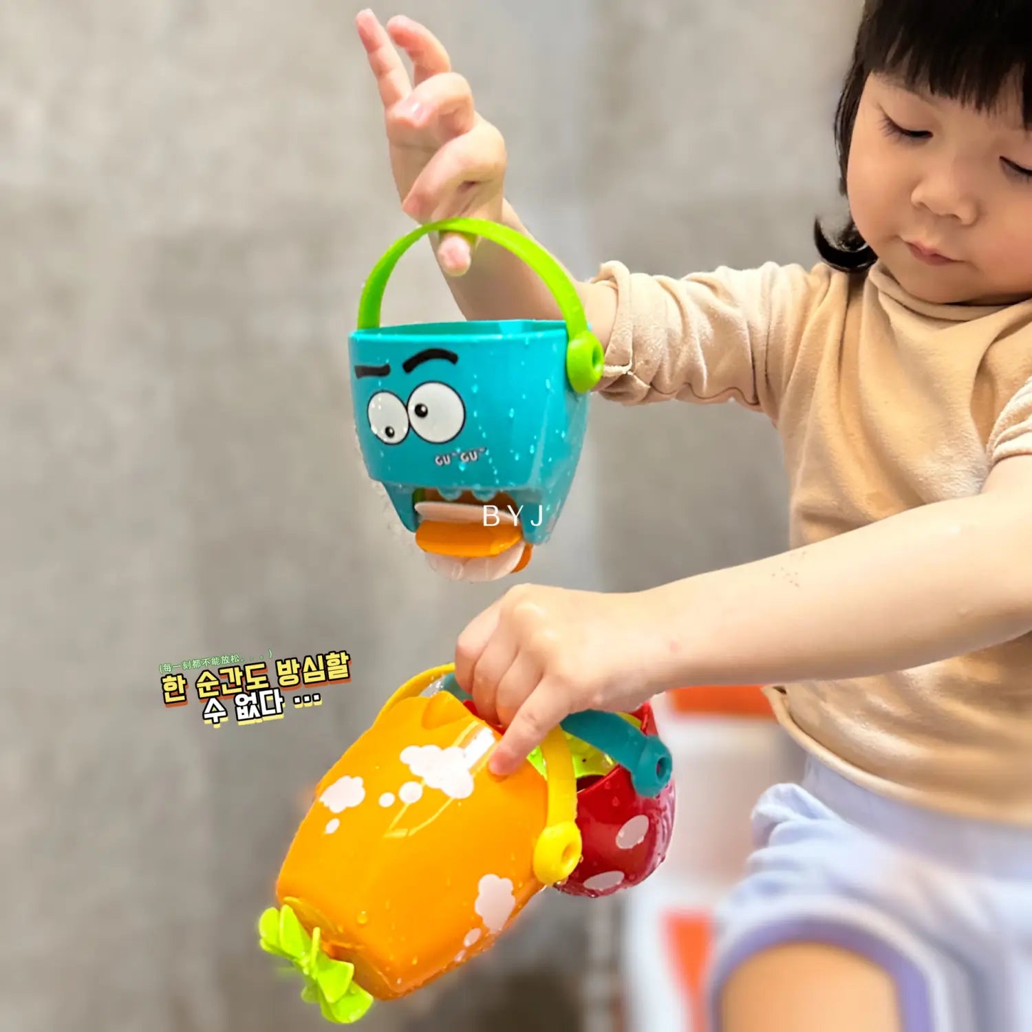 Ein blauer und orangefarbener Kunststoff-Badewannen-Eimer für Babys mit grünem Griff und Cartoon-Gesichtsdesign für ein Wassersprühspielset.