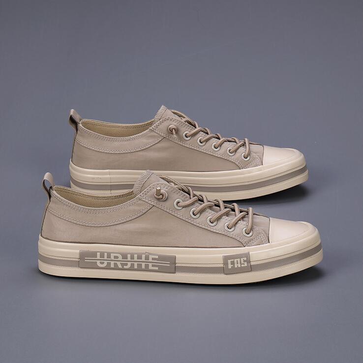 Baskets décontractées basses en toile beige pour hommes, avec une coque en caoutchouc blanc et une semelle, présentant une bande de logo grise conçue comme des chaussures d’été légères.