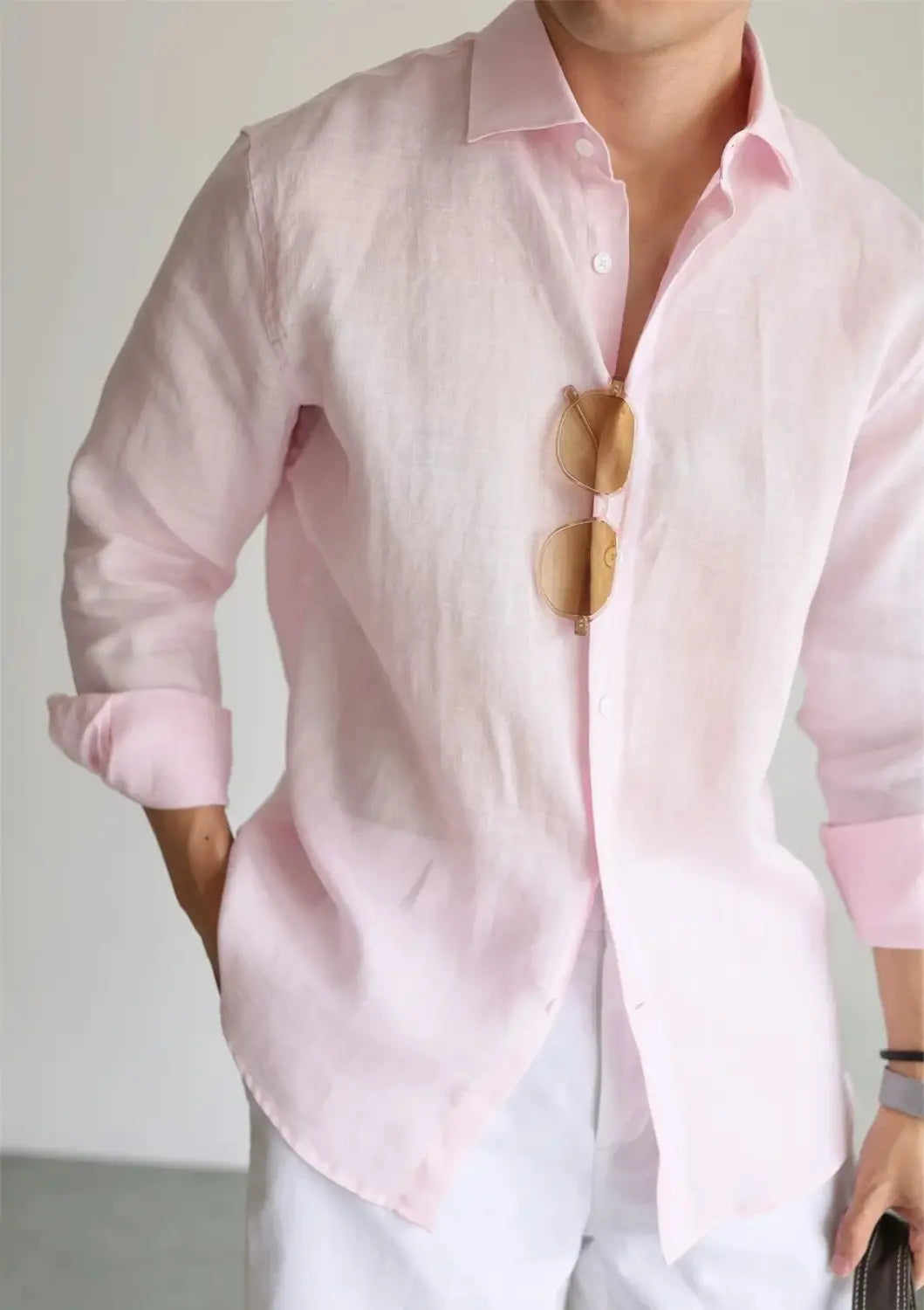A soft pink men cotton linen casual button down shirt with rolled-up sleeves and sunglasses resting on the chest.