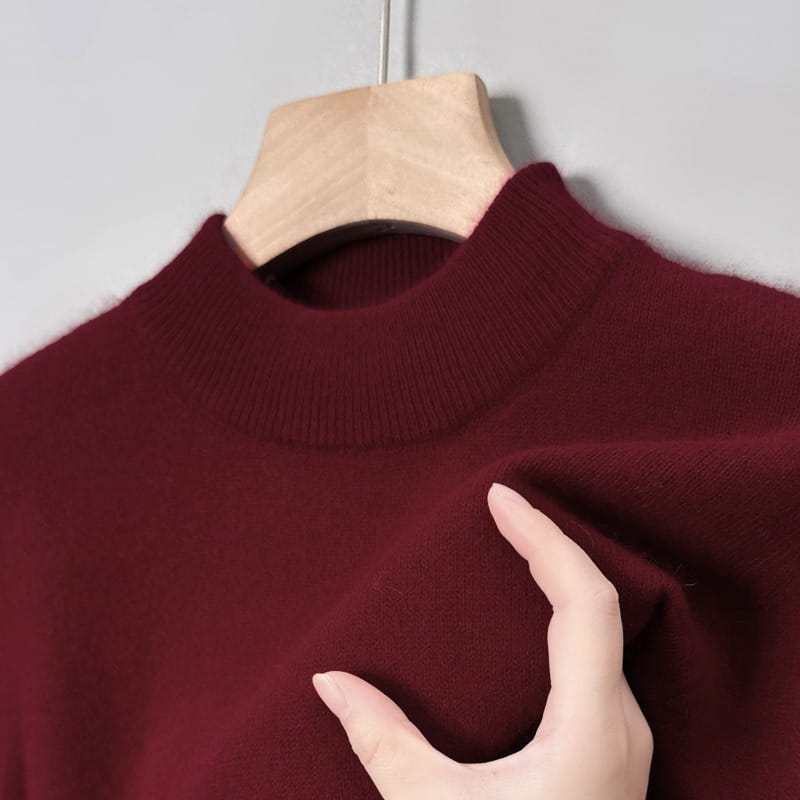 Ein edler weinroter Herren-V-Ausschnitt-Strickpullover mit einem weichen, gerippten Rundhalsausschnitt hängt an einem Holzkleiderbügel und eignet sich für lässige Winterkleidung.