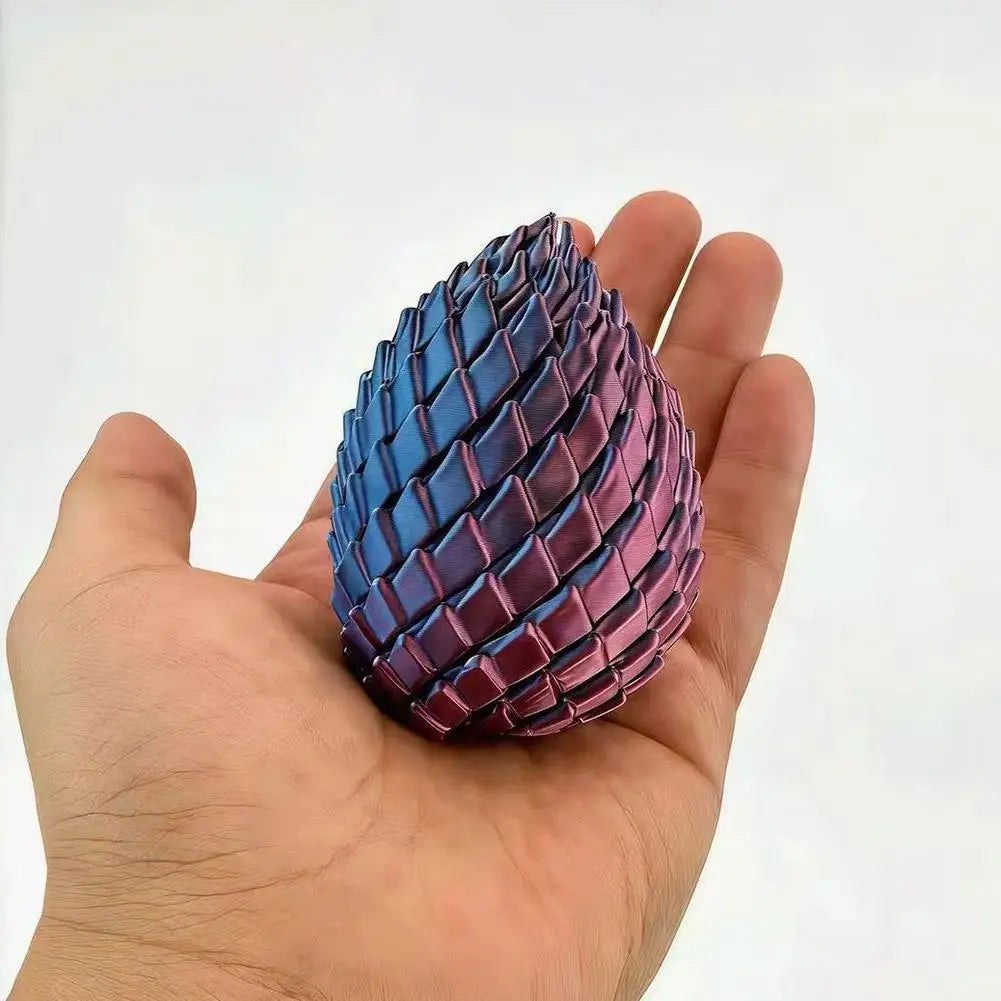 A hand holds a small articulated dragon egg fidget toy with a metallic gradient from blue to deep purple.