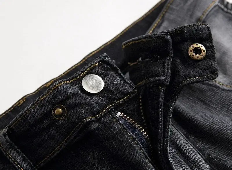 Jeans de moto pour hommes, coupe slim délavée, en denim foncé, avec une braguette à bouton classique, et des éléments métalliques dans un ton laiton et argent contrastés.
