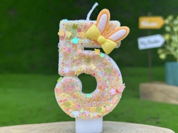 A glitter bunny ear number five birthday candle in pastel colors featuring a yellow bow and glittery finish.