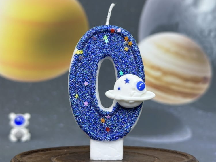 Una vela azul con brillo con el número cero para cumpleaños, con un dije de nave espacial blanco adherido, utilizada como adorno para pastel de fiesta planetaria.