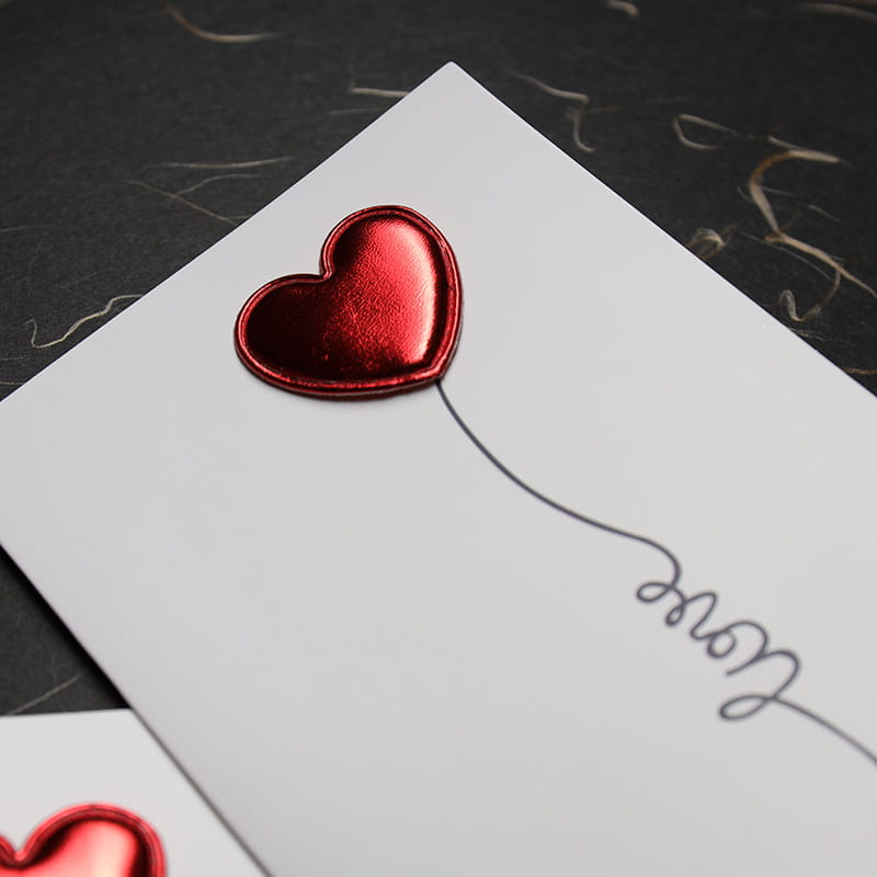 a shiny red metallic heart-shaped sticker on a white card for red heart valentine greeting cards wedding invitations