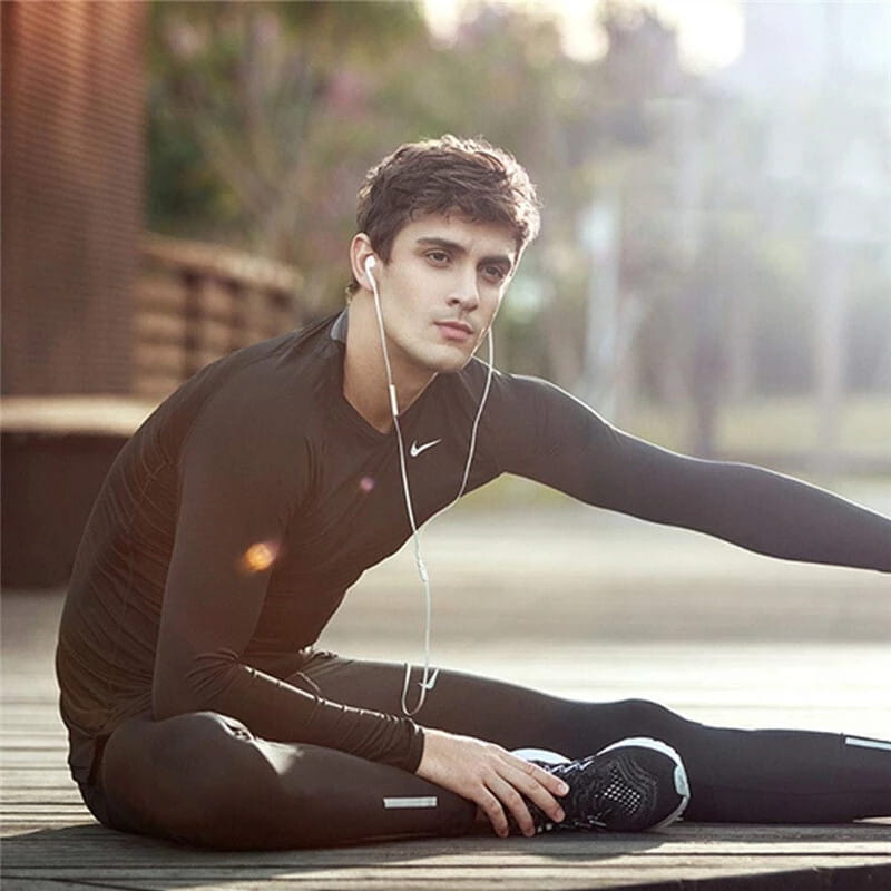 Haut de sport long Nike noir à manches longues avec un logo « swoosh » blanc discret sur la poitrine, présenté avec des écouteurs filaires pour iPhone avec des connecteurs USB C et Lightning.