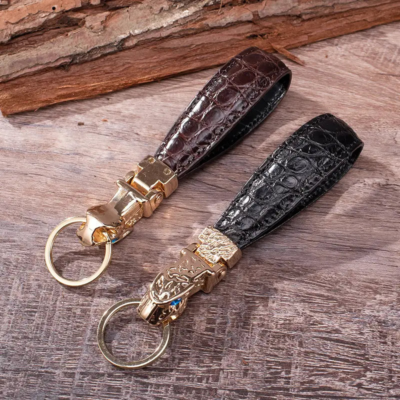 Two crocodile-embossed leather keychains in dark brown and black with gold-toned engraved tiger head clasps for luxury car key rings.