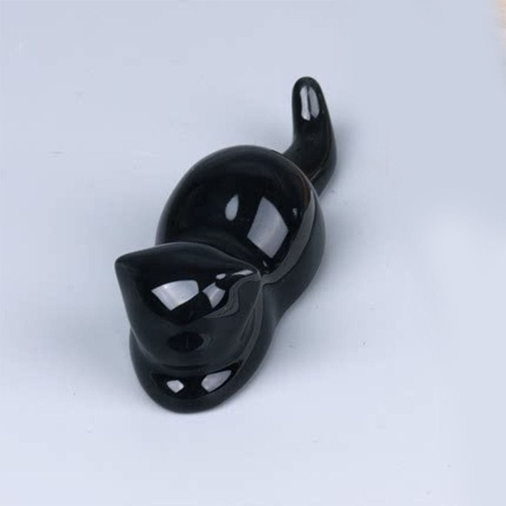 A glossy black ceramic pen holder and minimalist calligraphy brush rest in the shape of a cat lying on its side.