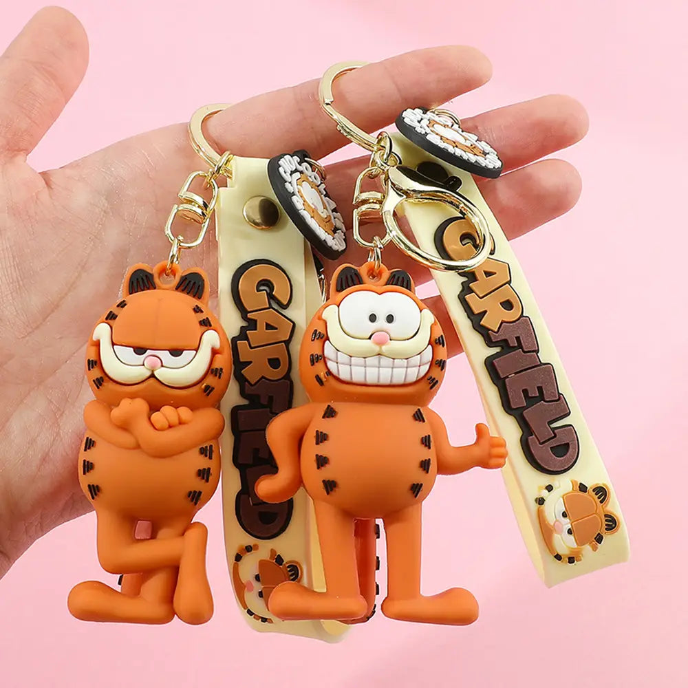 Orange garfield keychain rubber anime cat key pendant with black whiskers and stripes attached to beige straps featuring the garfield logo in brown lettering.