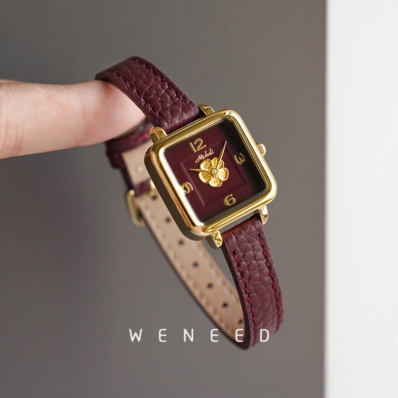 A square-faced women quartz watch with a gold-tone case, burgundy textured leather strap with visible stitching, and a maroon dial featuring a golden floral motif.