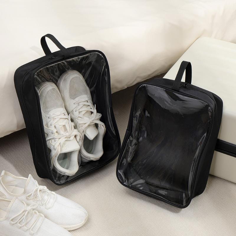 Sac de voyage imperméable noir pour chaussures fabriqué dans un matériau durable, avec panneau frontal transparent et poignée supérieure ; un sac contenant des baskets blanches pour un rangement pratique à fermeture éclair.