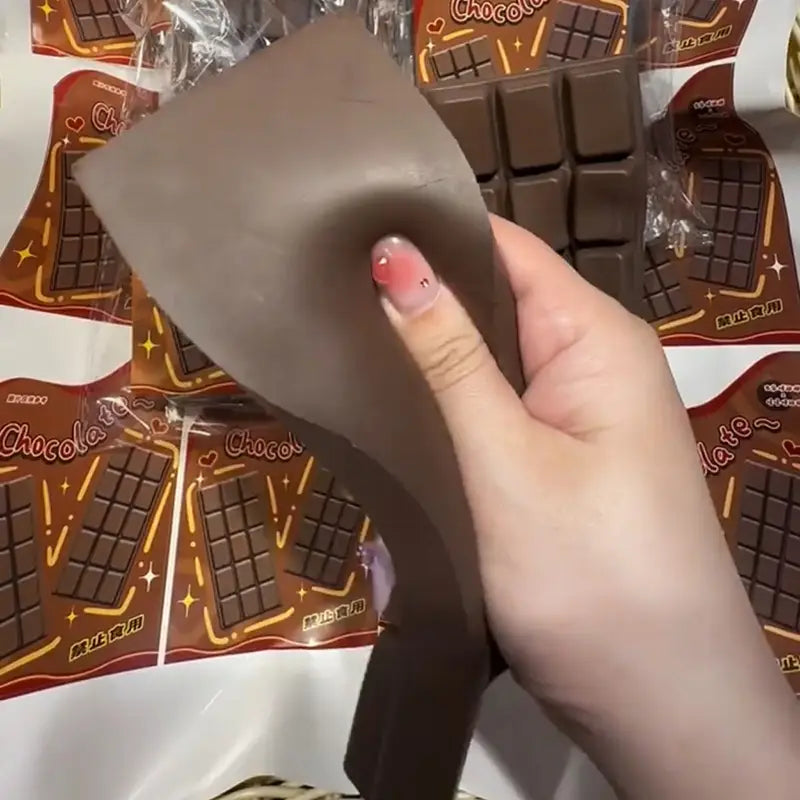 A flexible matte brown chocolate bar squeeze toy with a slightly textured surface and molded grid lines designed as a slow rising sensory fidget.