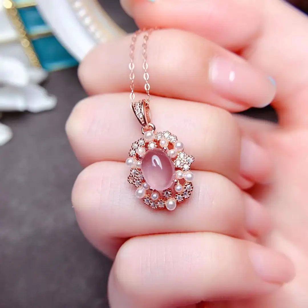 Un pendentif délicat en or rose, avec une pierre de jade rose ovale au centre, entourée de diamants et de perles, provenant d’un ensemble de bijoux en argent sterling avec quartz rose.