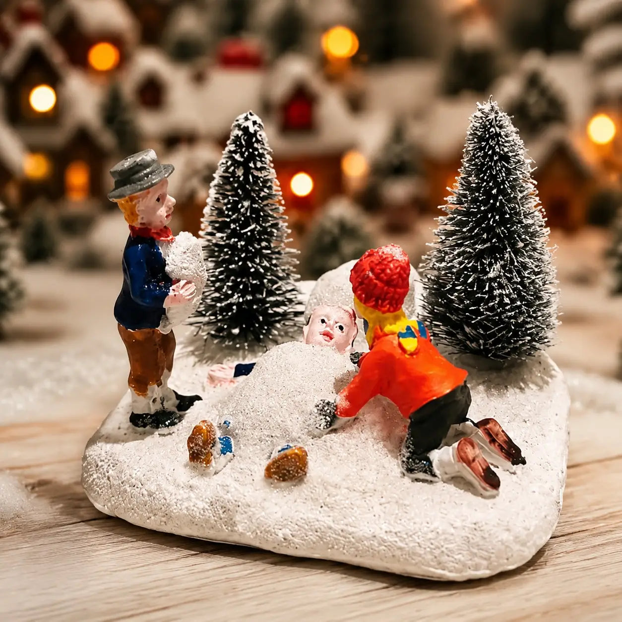 Set mit Weihnachtlichem Dorf-Figürchen „Kinder spielen mit Schnee“: mit drei farbenfrohen Mini-Figuren und bereiften Bäumen auf einer strukturierten verschneiten Basis.