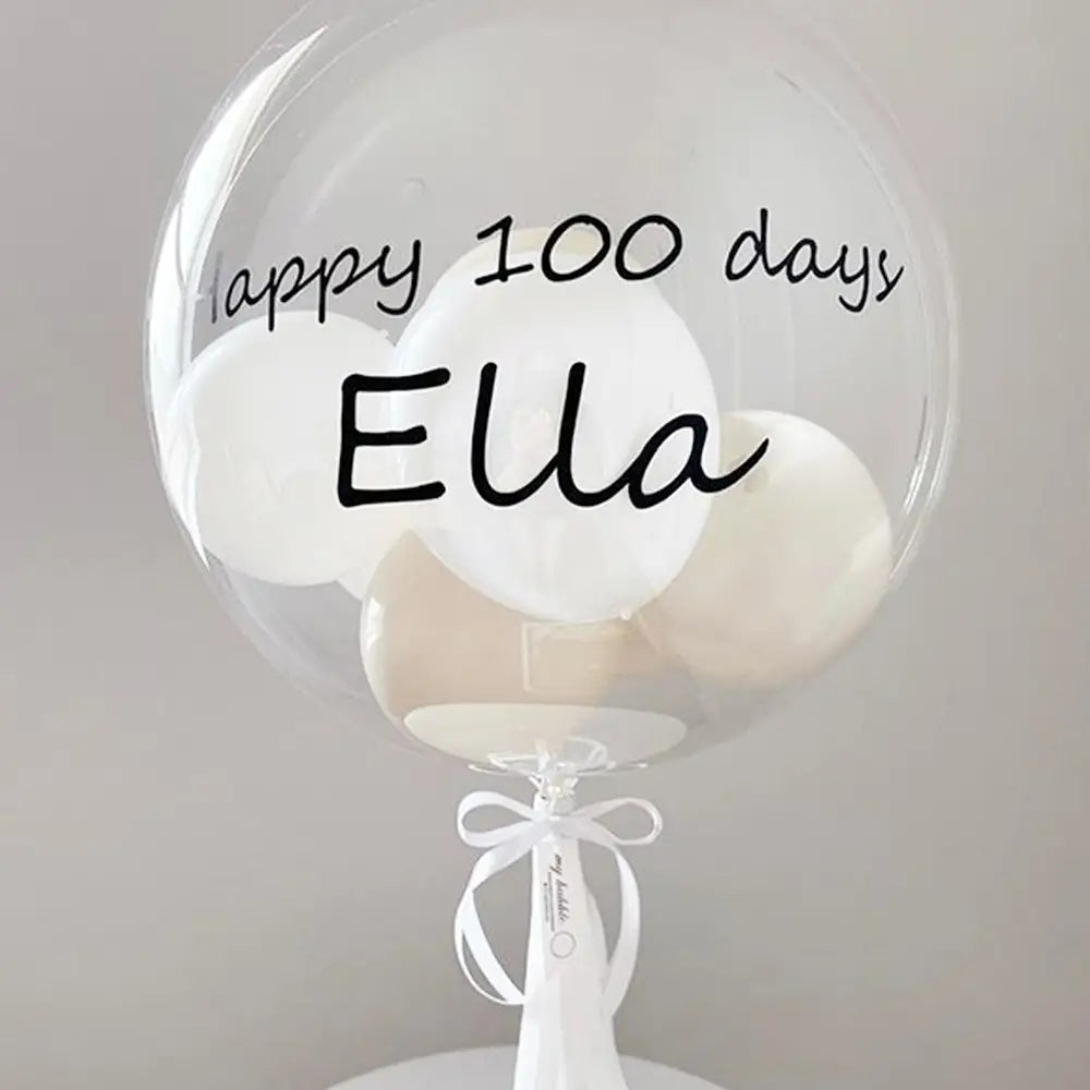 Transparenter 36-Zoll-Bobo-Ballon mit individuell handschriftlich in Schwarz „Happy 100 Days Ella“-Text und weißen Ballons im Inneren, gebunden mit einer weißen Schleife, mit einem individuellen Baby-Party-Ballonaufkleber.