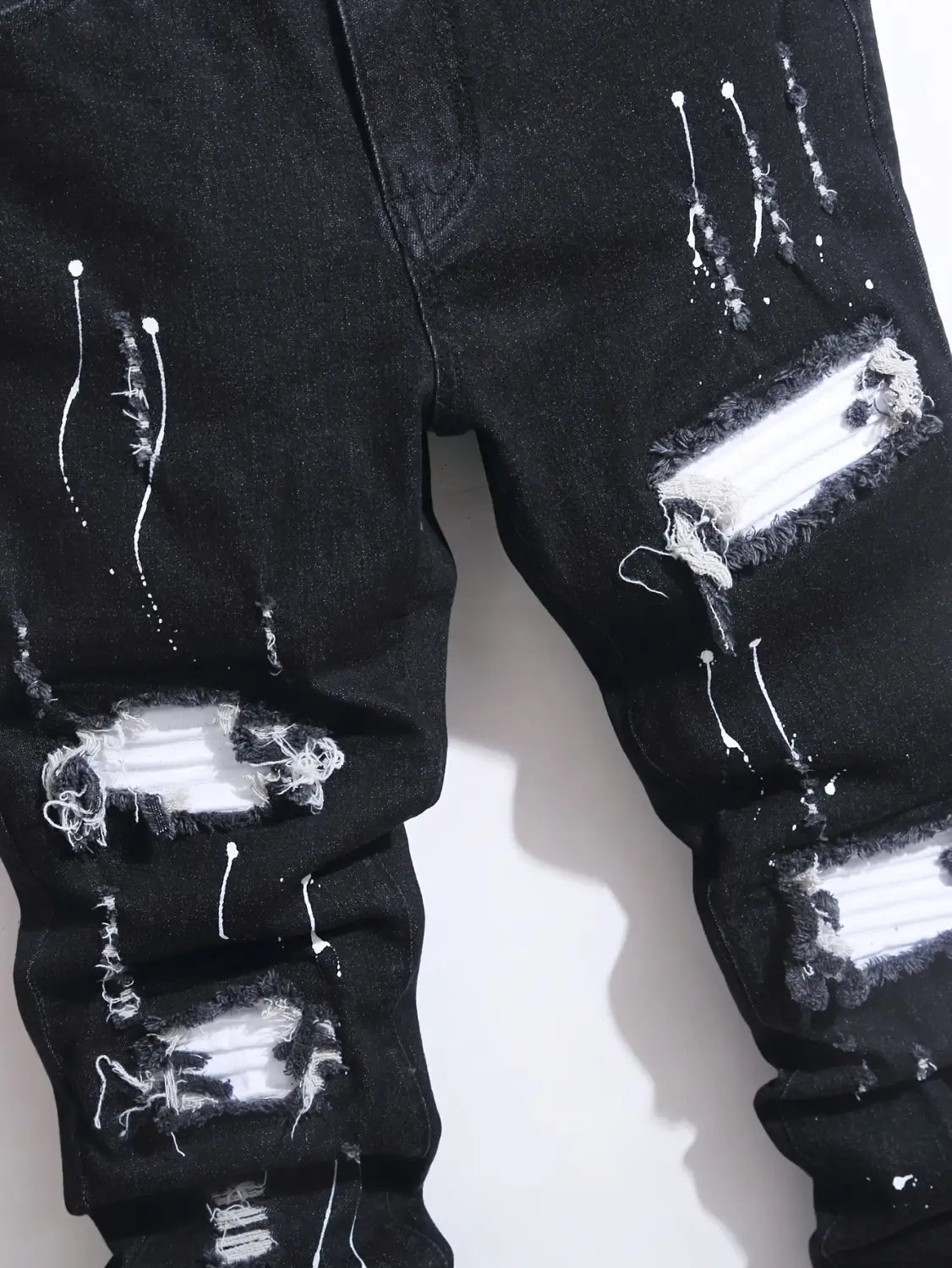Herren-Ripped-Skinny-Bikerjeans in schwarzem abgetragenem Denim mit weißem Farbspritzer-Design und zerrissenen Details für den Streetwear-Stil.