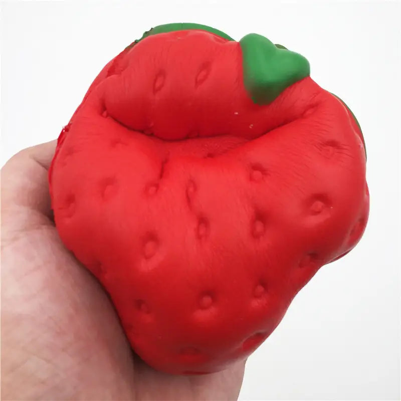 Un juguete antiestrés de fresa con forma de fresa, de textura roja y elevada lentamente, blandamente esponjoso, con una parte superior de hojas verdes.