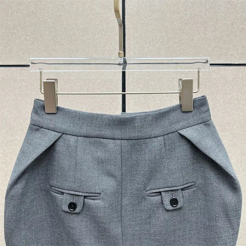 Jupe crayon grise taille haute de longueur genou au style Y2K présentant un tissu gris texturé et deux poches à rabat frontales, chacune fermée par un bouton noir.