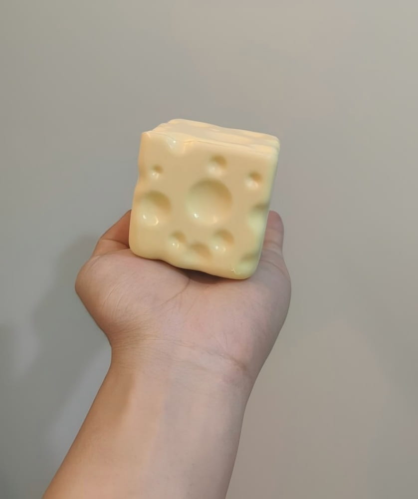 ein blassgelber, würfelförmiger Käsewürfel-Stressball mit charakteristischen Löchern, gestaltet als knetbares Sinnes-Plaything