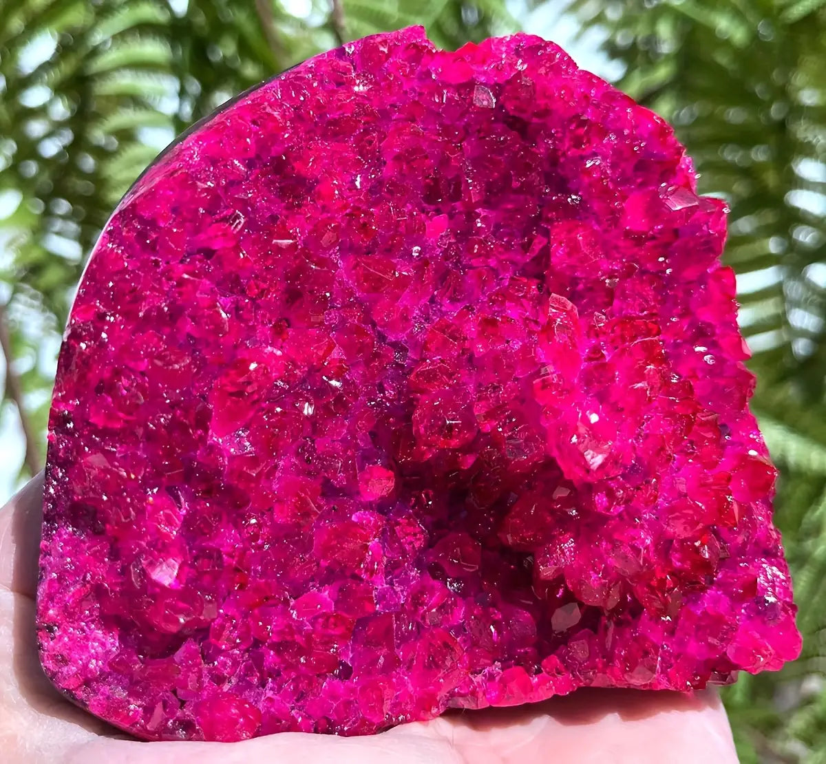 Décoration intérieure pour maison avec un amas de cristaux de géode en quartz rose, présentant une surface cristalline rugueuse rouge fuchsia éclatante, avec des facettes translucides.