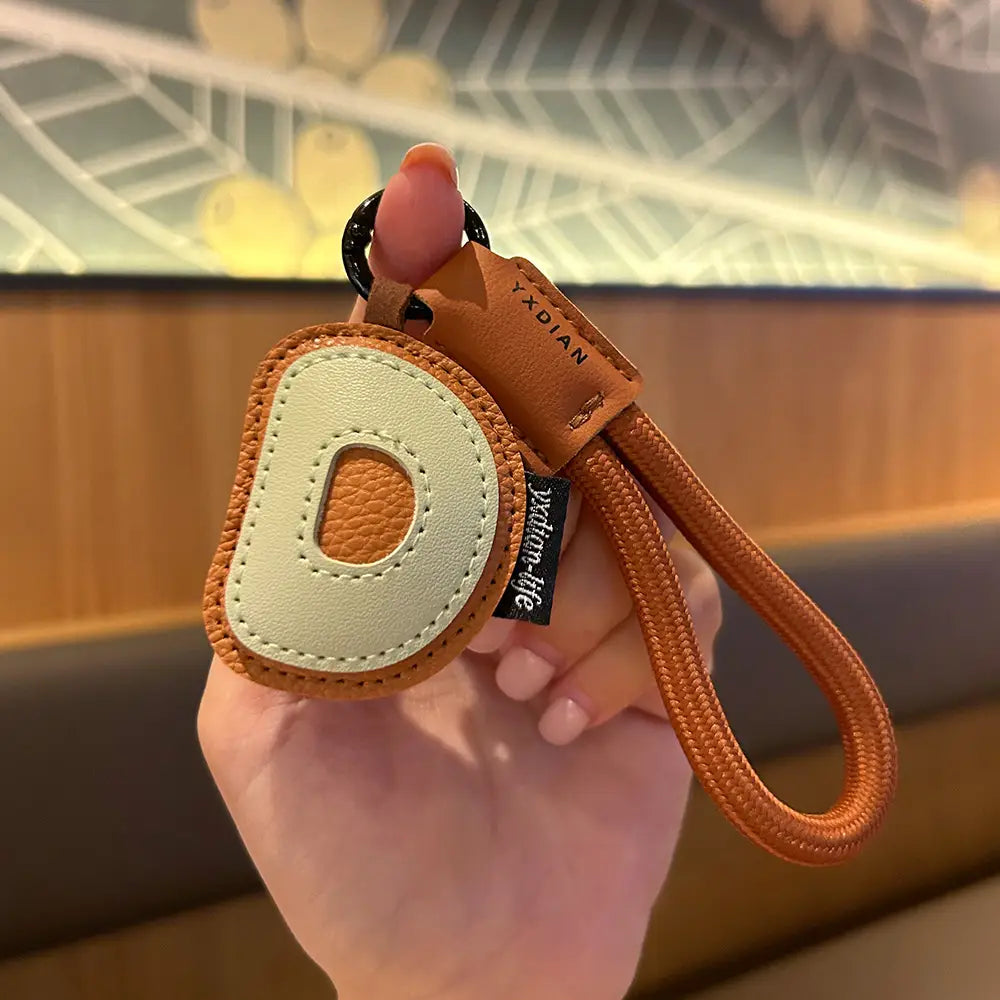 Tan leather initial keychain with a cream-colored letter d patch and braided orange strap wristband charm.