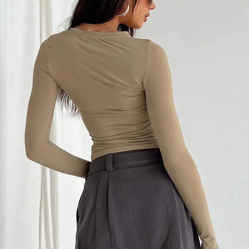 Blusa corta ajustada tipo slim fit color topo para mujer, con mangas largas fruncidas, cuello alto, mostrada desde la parte posterior.