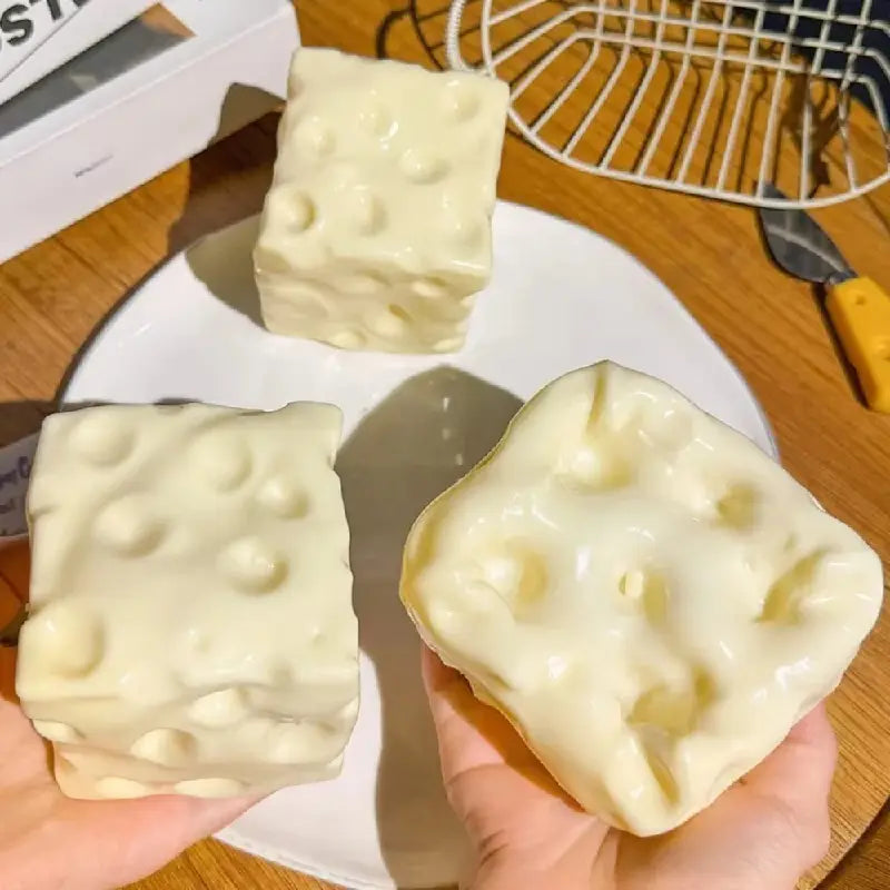 Cremefarbenes Käse-Soft-Glücksbringer-Spielzeug zur Stressreduktion, entworfen als käseförmige Badebomben mit strukturierter Oberfläche, die Löcher wie beim Schweizer Käse nachahmt.