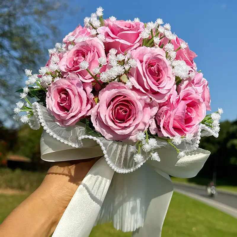 A delicate white silk rose wedding bouquet featuring pink artificial roses accented with white baby’s breath and tied with a lace-trimmed satin ribbon.