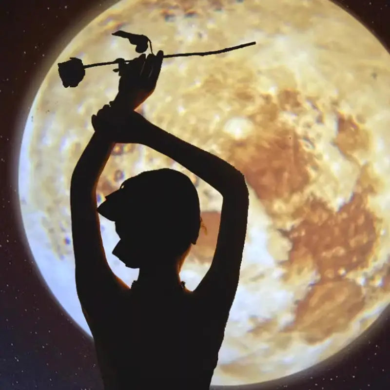 Silhueta de una persona que sostiene una rosa frente a una gran luna llena texturizada proyectada por una lámpara de proyección USB para luz de estrellas de galaxia de luna y Tierra.