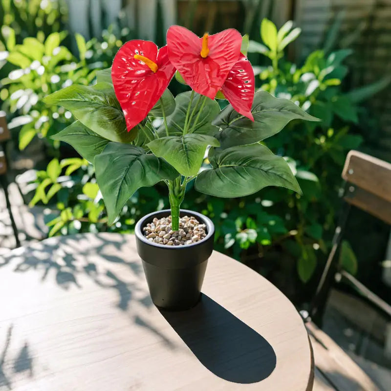 Artificial red anthurium potted plant with vibrant red flowers and glossy green leaves in a sleek black ceramic pot.