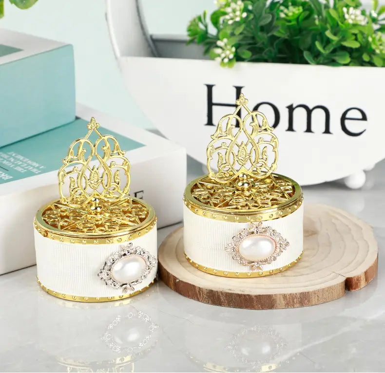 Boîte à bonbons de mariage cylindrique dorée blanche, avec bordure dorée et un couvercle en filigrane orné, agrémenté d’une perle centrale, enchâssée dans un décor à strass argentés ; contenant une perle-bonbon décorative.