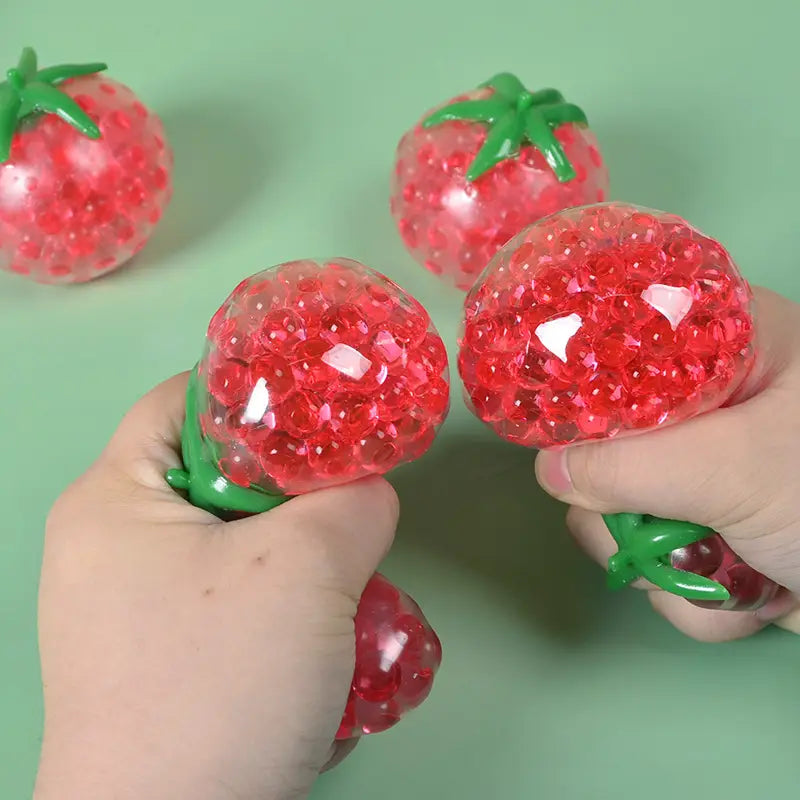 Red strawberry-shaped squishy tomato stress relief toy made of clear gel beads with green plastic stem designed as a squeeze ball.