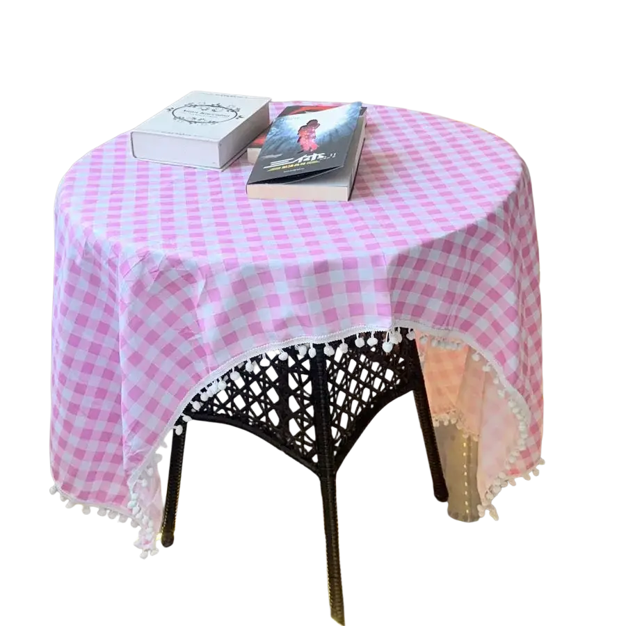 Se muestra una mantelería a cuadros rosa y blanca con un ribete de pompón desde una vista superior en una imagen de producto titulada «mantelería con ribete de encaje de lunares rosa».