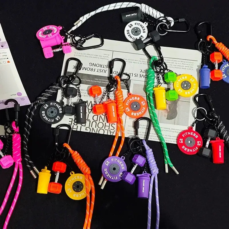 A vibrant collection of fitness keychains featuring colorful plastic dumbbell and weight plate charms attached to braided cords, designed as gym bag charm accessories.