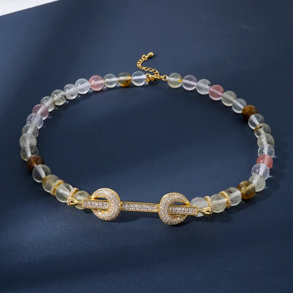 Un delicado collar tipo choker con cuentas que presenta cuentas de piedras preciosas claras rosadas y marrones, con un broche de tono dorado adornado con cristales brillantes de circonita cúbica.