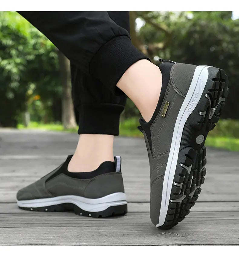 Men orthopedic slip-on walking shoes in gray and black with a white midsole, rugged tread pattern, and outdoor branding on the side designed for outdoor use.