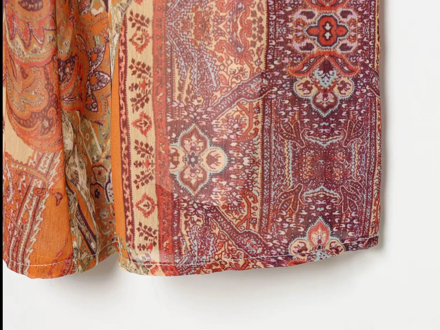 Jupe midi à imprimé cachemire taille haute, fluide et semi-transparente, aux tons chauds d’orange rouille et de bordeaux, avec un motif richement détaillé.