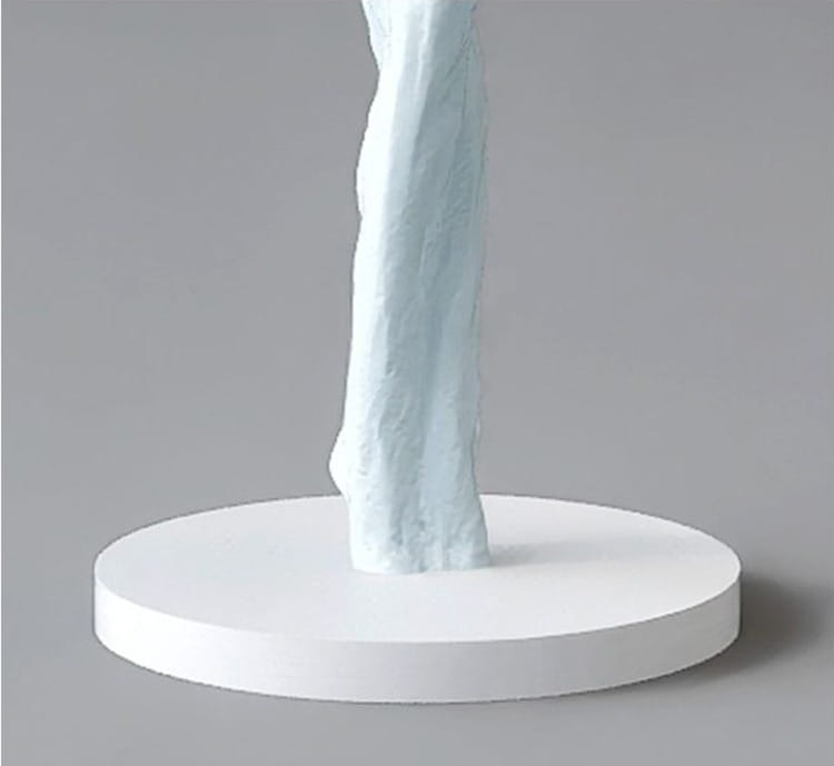 Une figurine de danseuse en résine bleu clair sculptée, à surface texturée, se tient sur une base circulaire blanche minimaliste mesurant 12x12x40 cm ; idéale pour une décoration intérieure moderne et des effets d'exposition.