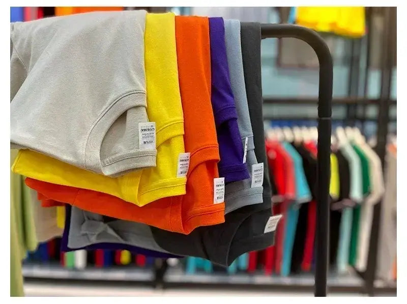 Une pile de t-shirts vintage à motif de voiture de muscle en coton uni et coloré, dans les tons gris, jaune, orange, violet et noir.